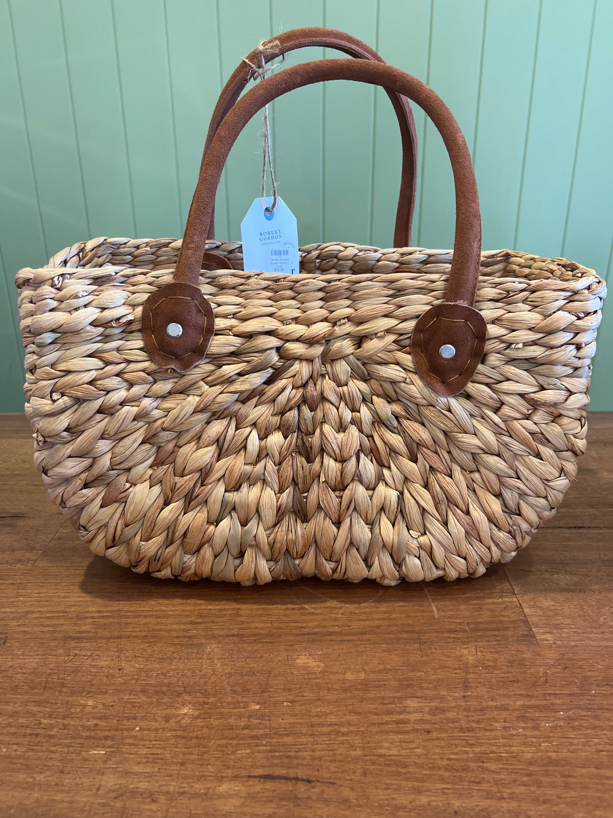 Woven basket with brown handles on a wooden surface against a green wall.